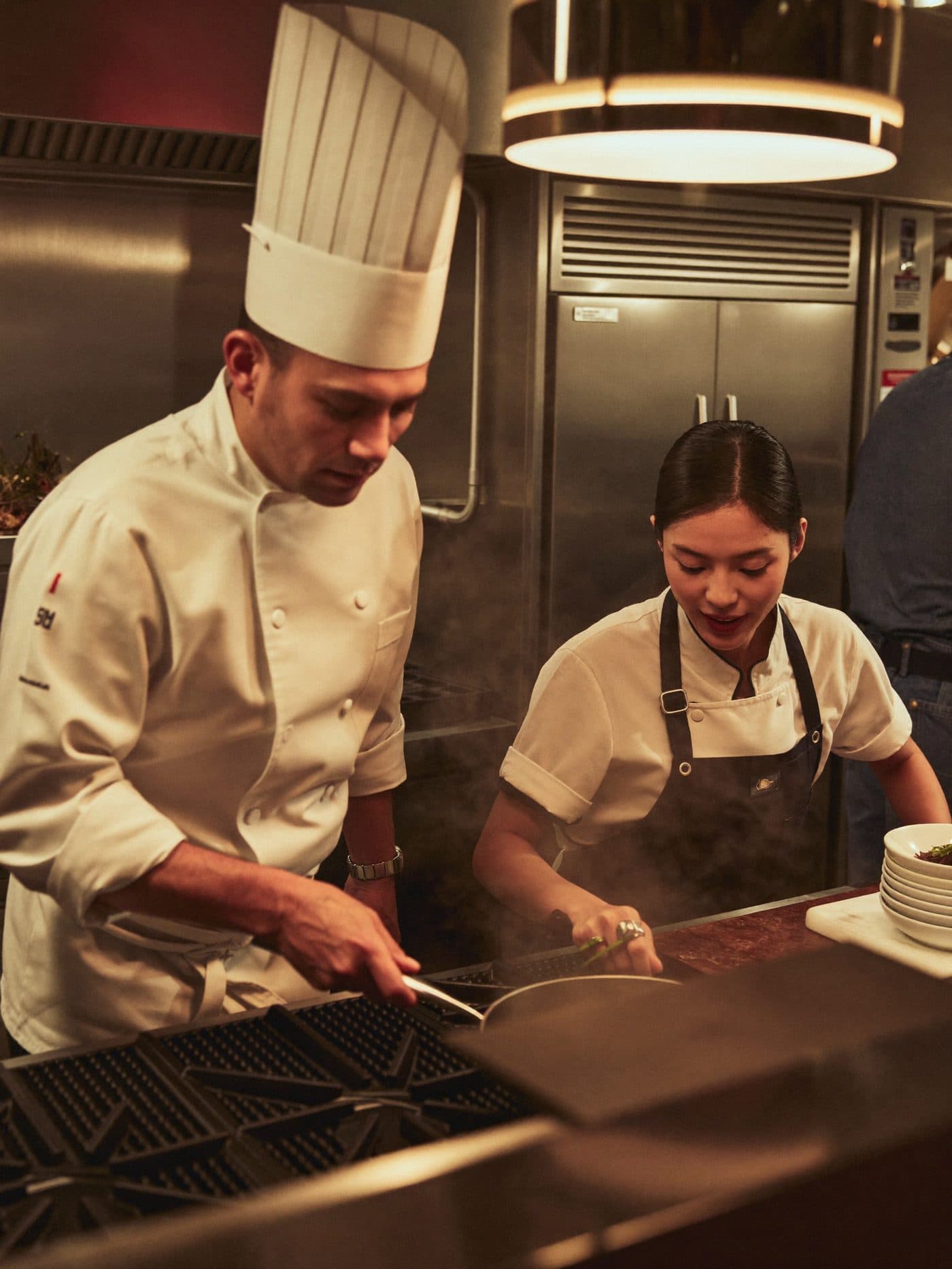 Head chef and line cook plating dishes together in a busy restaurant kitchen during service