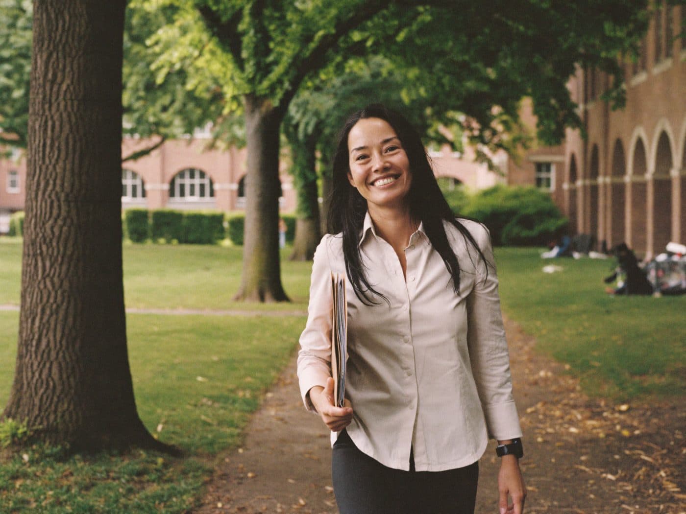 University administrator walking through a sunlit campus courtyard with a folder under one arm