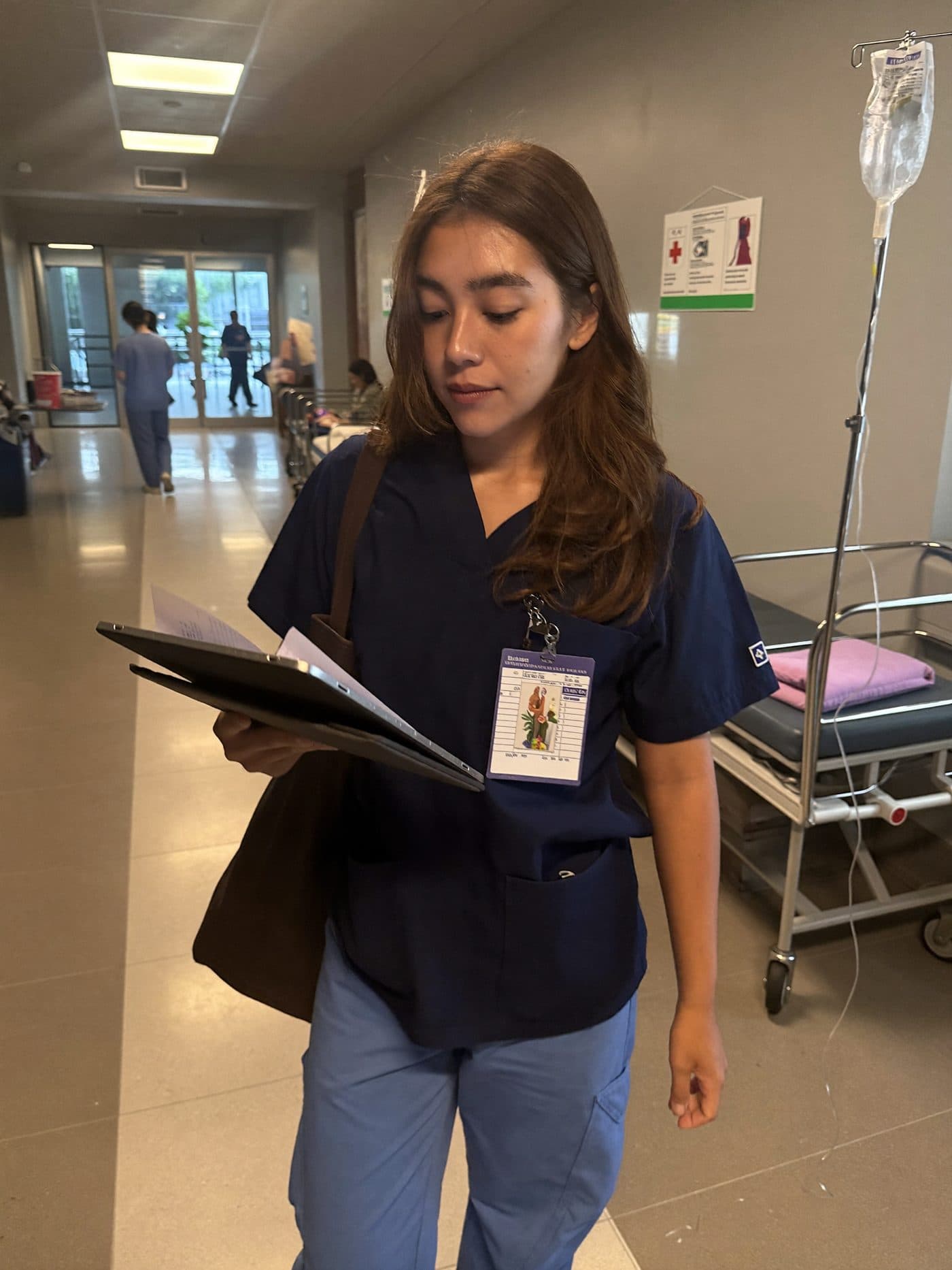 Nurse in navy scrubs at a nursing station checking the shift roster on a tablet